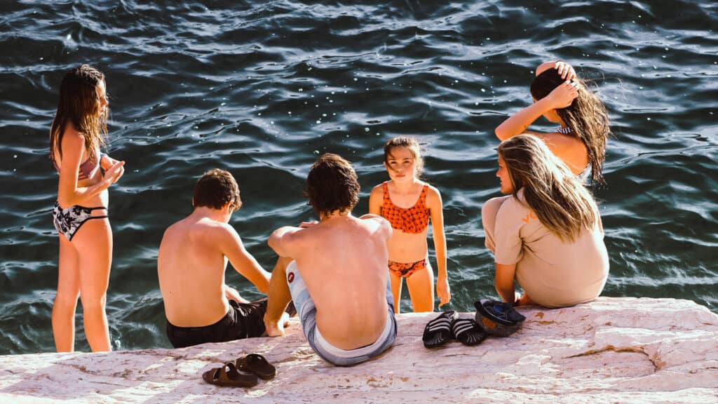 1920x1080 photo of a group of kids sitting by the edge of a lake on a warm summer day