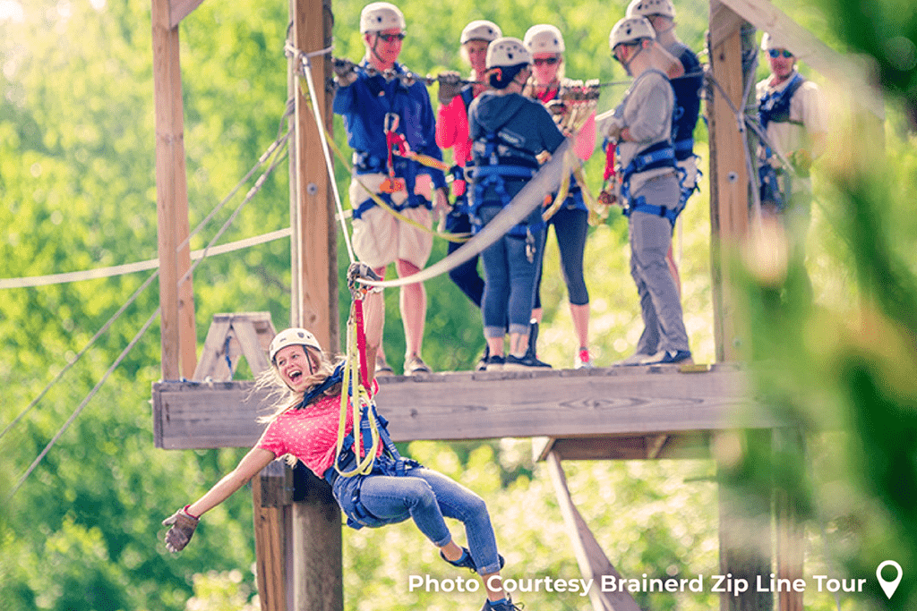 1200x800 photo of woman going ziplining at Brainerd Zipline Tour with a group of happy people in the background on a platform in the air with trees behind them