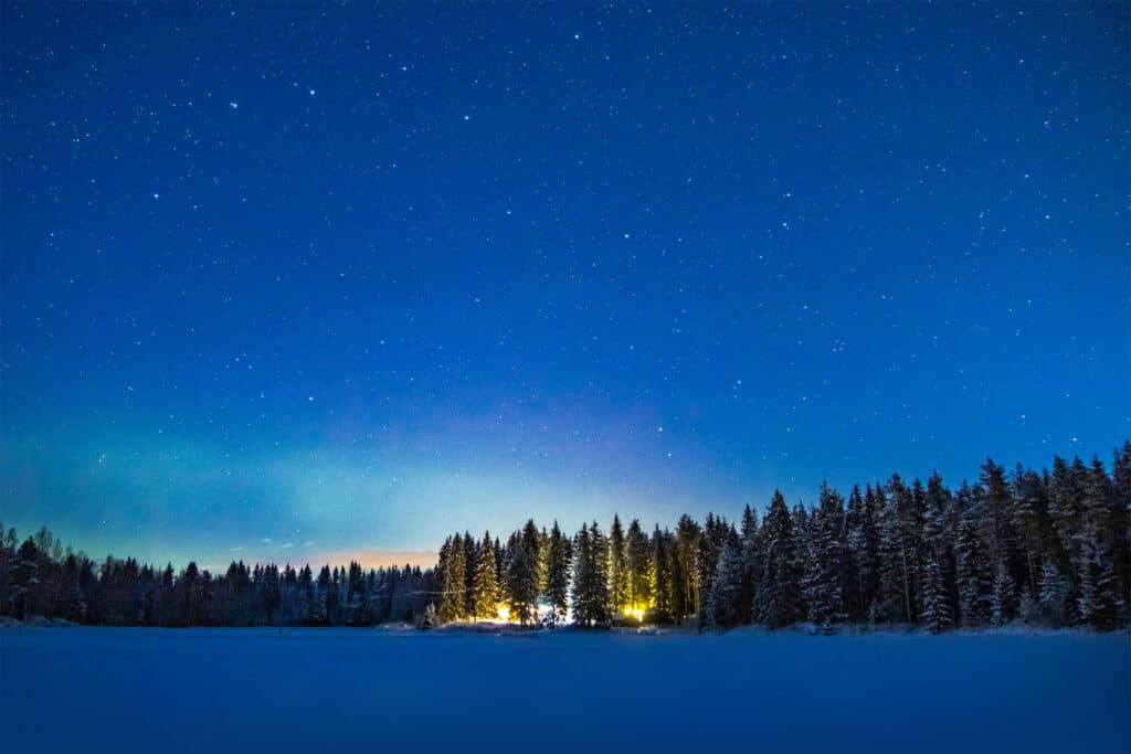 1920x1280 photo taken in the evening from the middle of a frozen lake with a cabin at the edge of the lake surrounded by pine trees