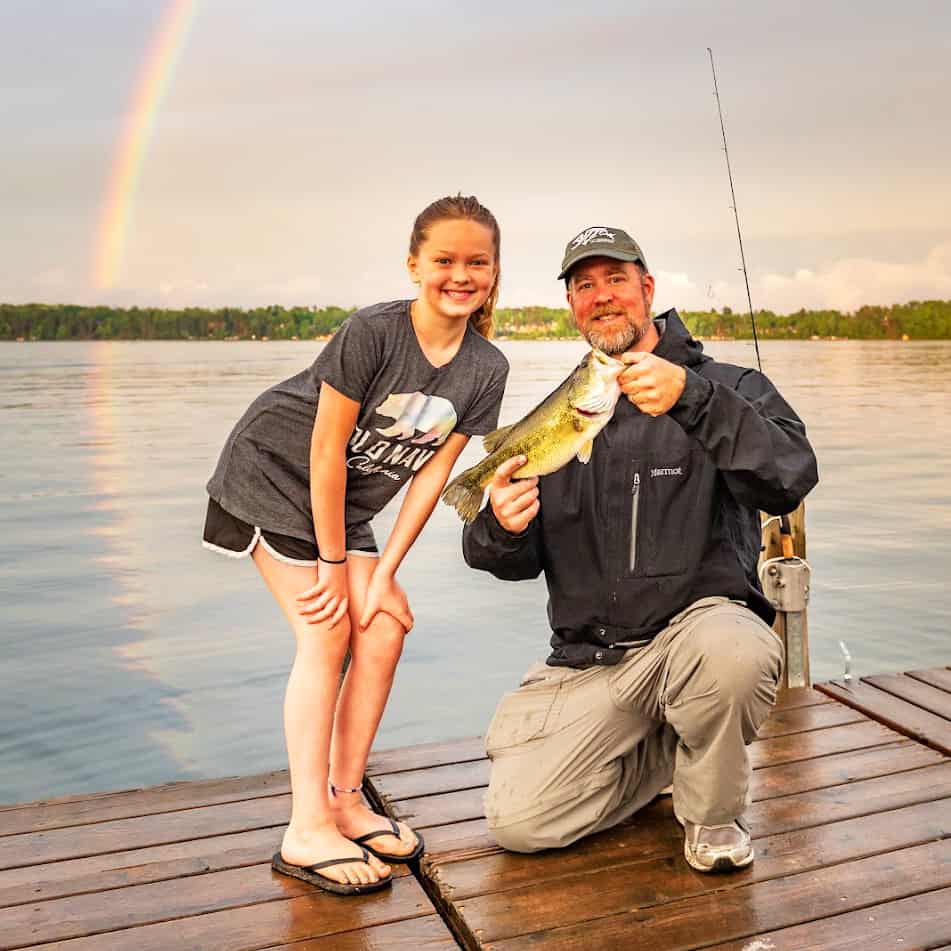 Square Photo of a dad and daughter fishing off a dock at Craguns Resort with a rainbow in the background