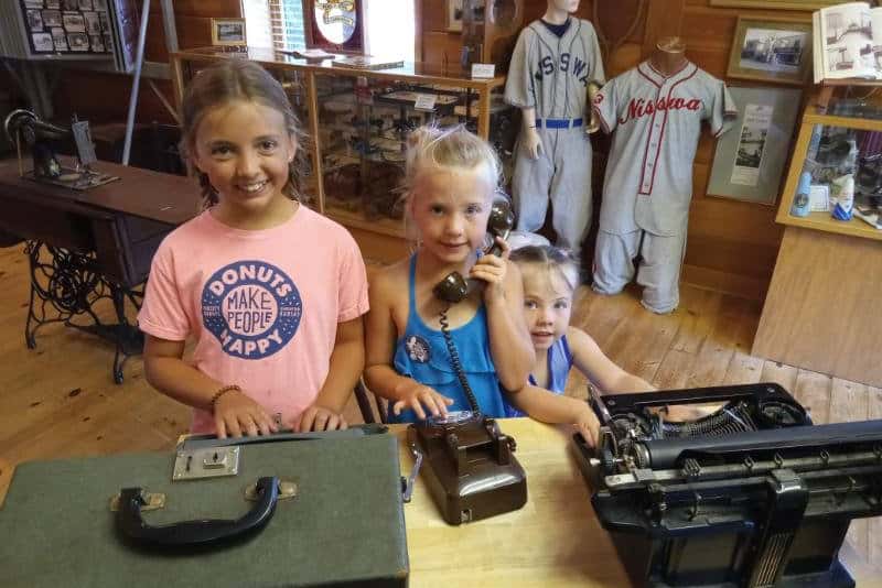 Photo of three smiling little girls in a hisotric log cabin museum