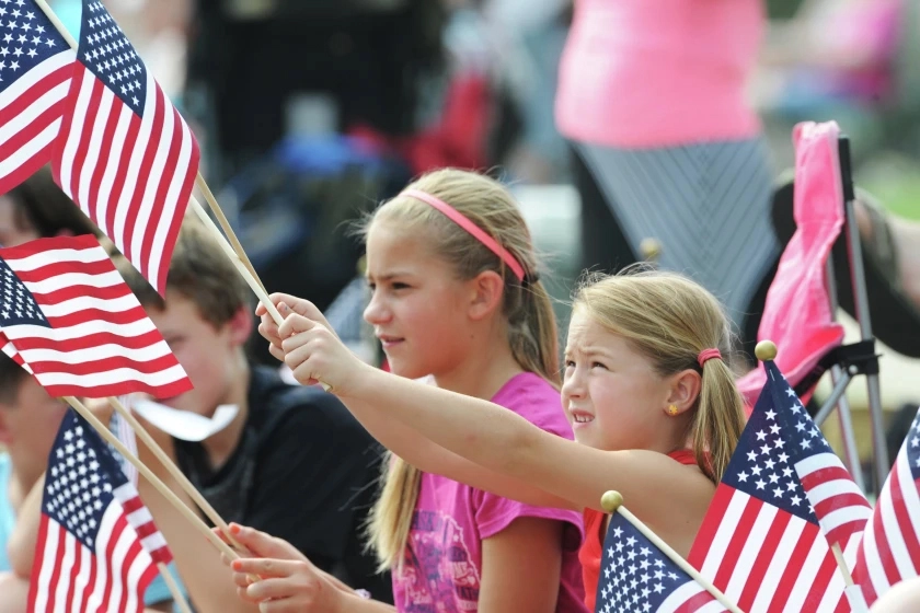Two girls waving American flags in a crowd of people Fourth of July Parade