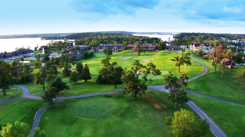 Aerial photo of Maddens on Gull Lake on a summer day showing the vast golf courses with trees and walking paths with the large resort buildings and cabins in the distance and Gull Lake in the background