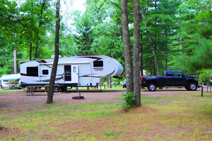 Photo of a truck and a large RV parked in a camping site surrounded by pine trees at the Cross Lake Recreation Area.