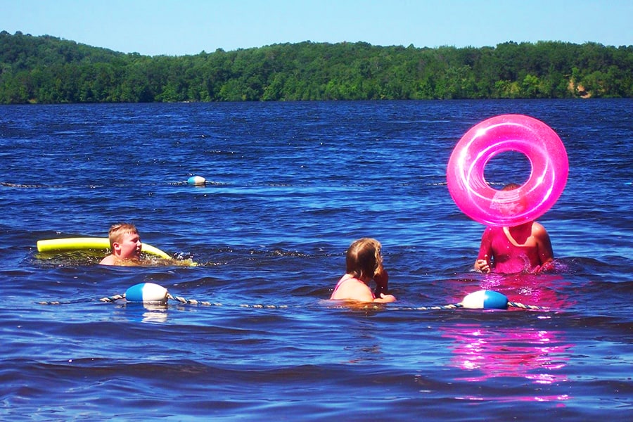 Photo of children swimming in a lake on a summer day with a far shore of forest