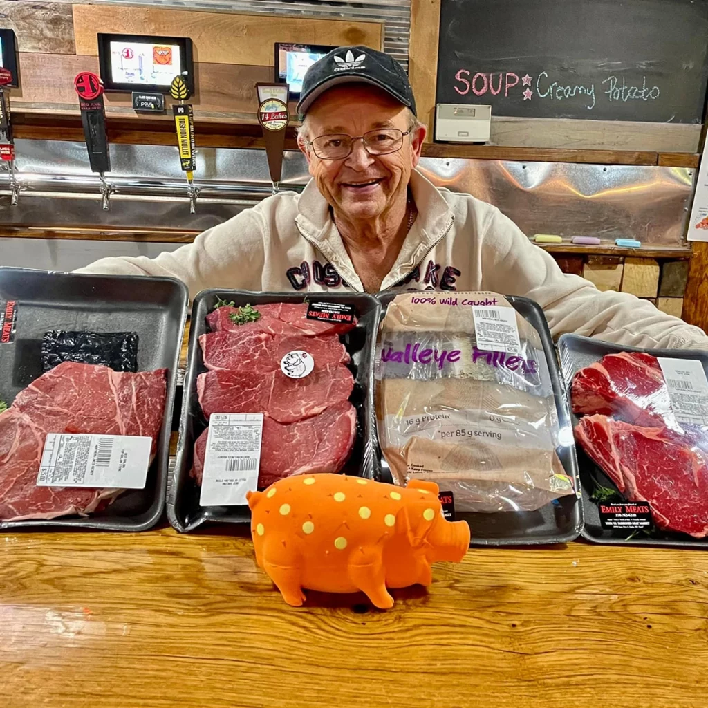 Photo of a an older man behind a bar counter holding packages of meat for a meat raffle at The Woods copy