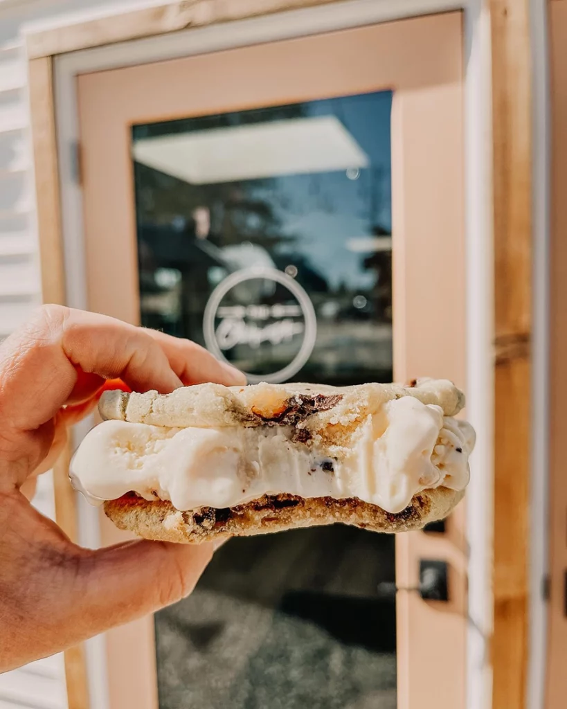 Photo of a person holding an ice creame sandwhich made with cookies and standing in front of a door to a shop copy