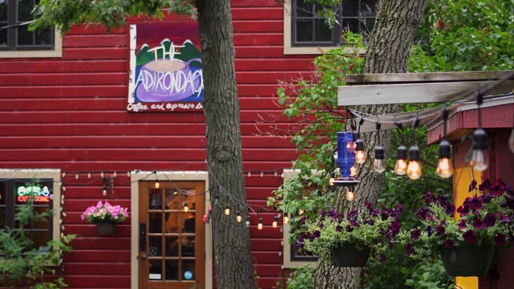 Photo of the front of a red building at Adirondack Coffee showing the hanging baskets and decor copy