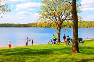 Photo of people swimming and biking at Whipple Beach with a lawn in the foreground and lake in the background on an early fall day.