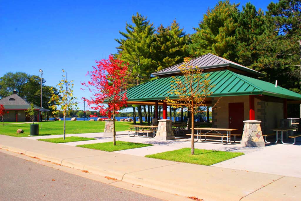 Photo of a picnic shelter and lawns with a lake in the background and trees at Whipple Beach on a bright summer day.