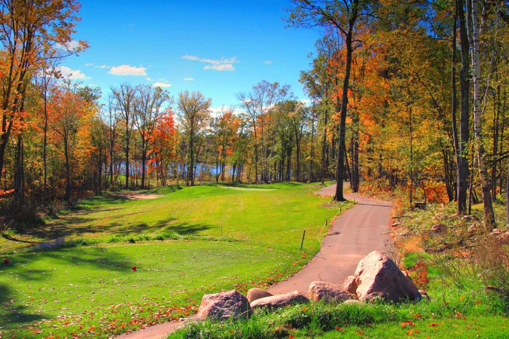 Crosswoods Golf Course on a sunny fall day with blue skys and trees with orange leaves and green grass and a lake in the background