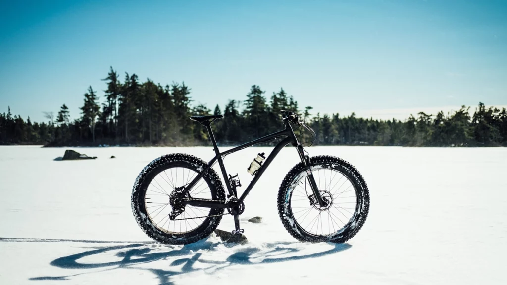 Photo of a fat tire bike on a frozen lake covered in snow with pine trees in the background on a sunny winter day