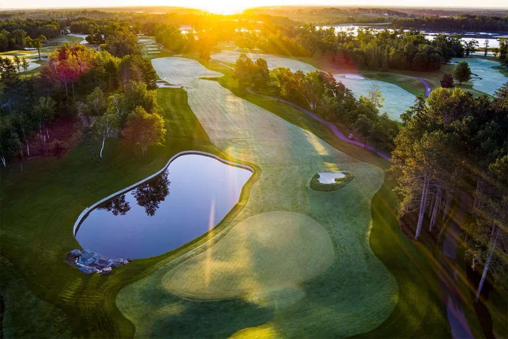Aerial photo of the golf courses at Cragun's Resort at daybreak showing huge golf courses surrounded by forest and a lake in the background