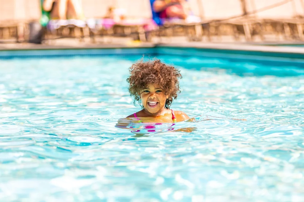 Photo of a little black girl swimming in a pool and smiling on a warm summer day at Grand View Lodge in Nisswa
