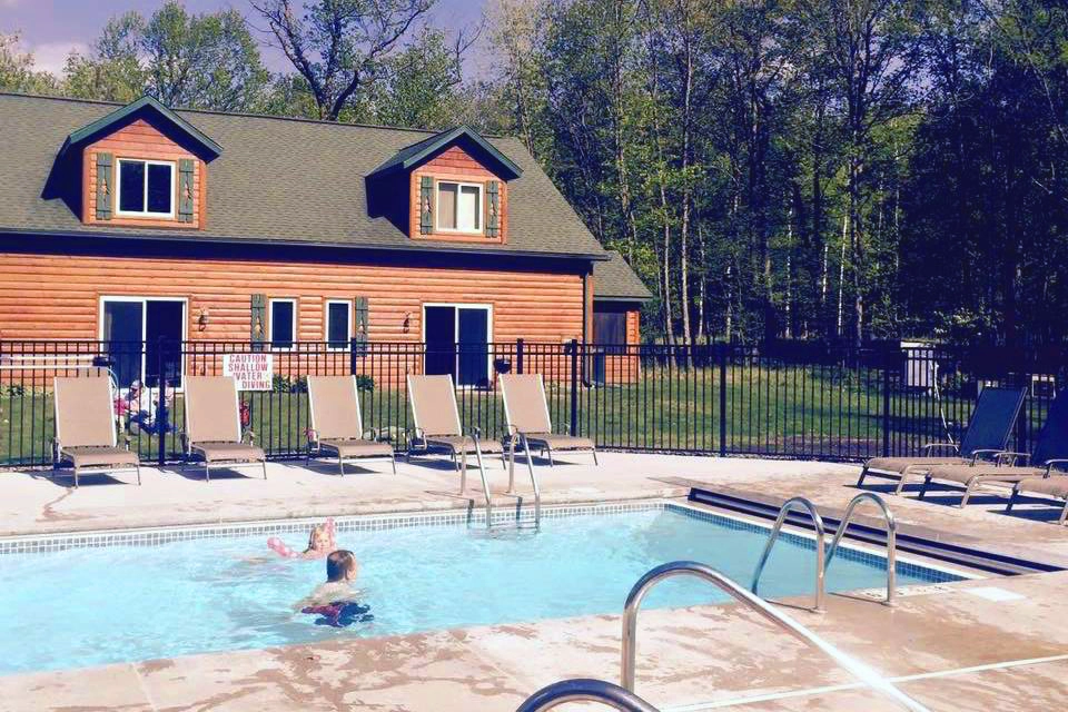 Photo of kids swimming in a pool next to a cabin at Woodland Beach Resort on a summer day copy