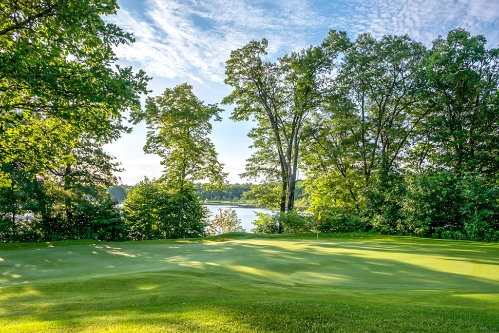 Photo of the golf course at Ruttgers Bay Lake Resort on a sunny morning with green grass and trees with a blue lake in the background
