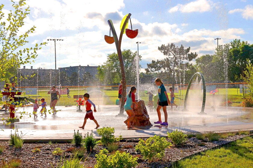 Photo of young kids playing at the Brainerd Splash Pad at Memorial Park on a summer day with parents watching from the edge of the splash pad