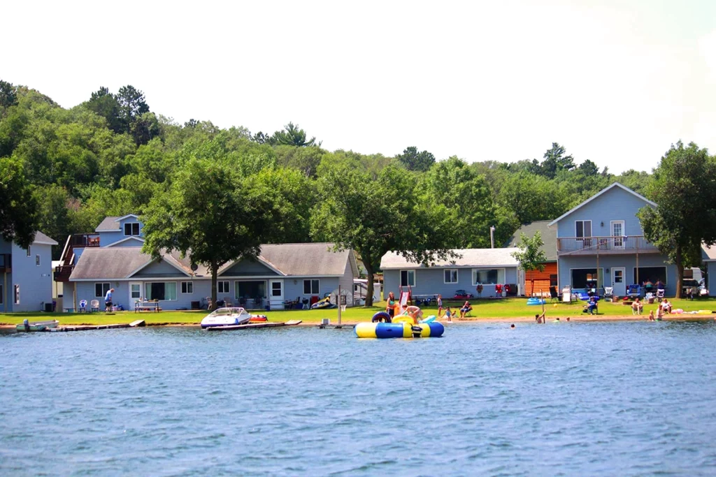Photo of Auger's Pine View Resort showing a huge sandy beach at the edge of a lake with cabins at the shore and kids playing in the lake
