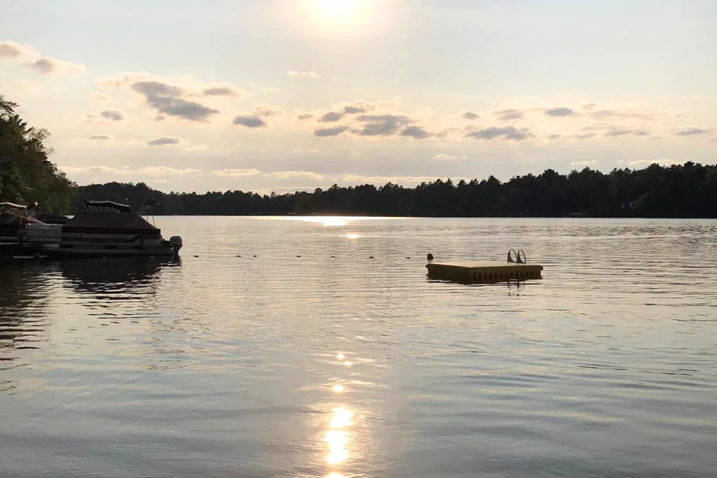 Photo of a lake at Fritz's Resort at sunset on a calm evening showing a small lake surrounded by forest with a swimming raft in the water