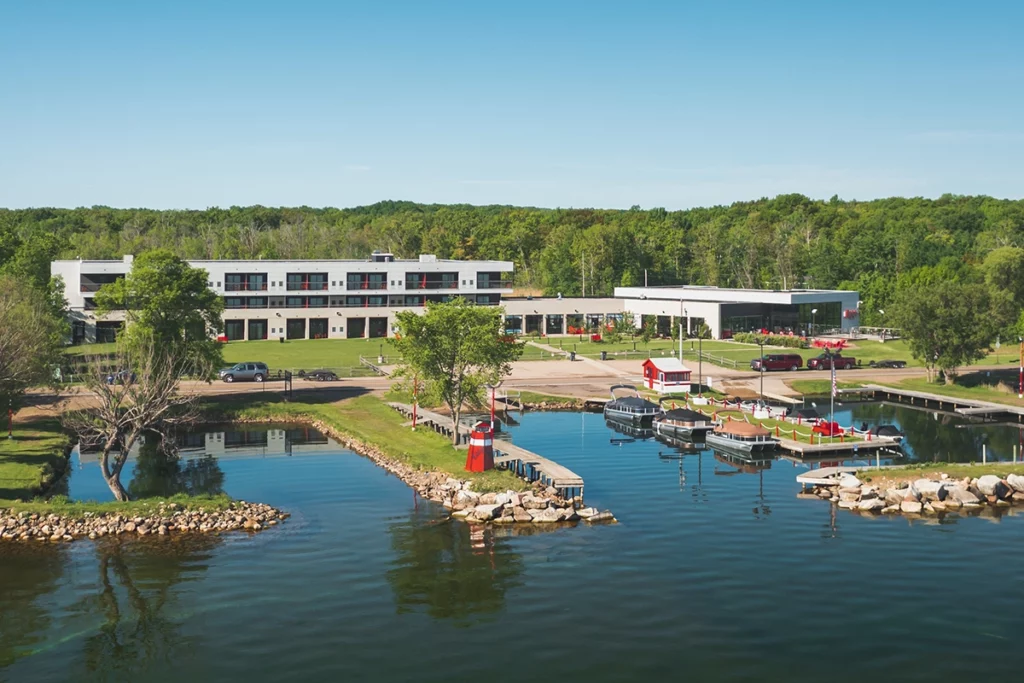 Photo of a modern hotel resort with forest in the background and next to a large lake showing big docks out front in the water on a sunny summer day copy