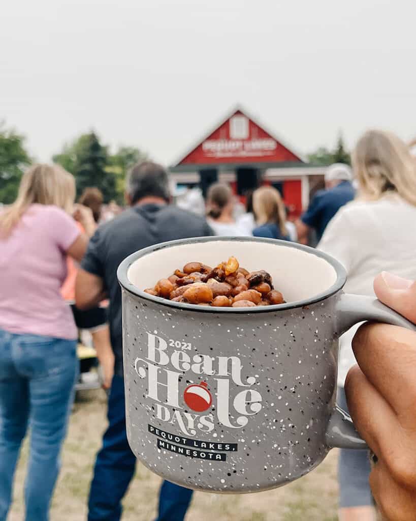 Bean Hole Days in Pequot Lakes showing gray mug filled with beans with a large crowed in the background