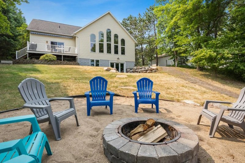 Love Lake Manor photo of vacation home rental of a large house at the edge in the summer with a sandy firepit and chairs in the foreground