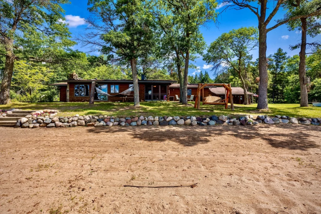 Photo of a cabin from Above and Beyond Homes called Lakeside Haven with a sandy beach in the foreground and trees in the background on a sunny summer day