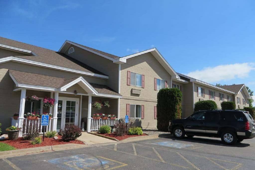 Photo of the exterior of the Country Inn in Deerwood showing a large, tan two story hotel on a summer day