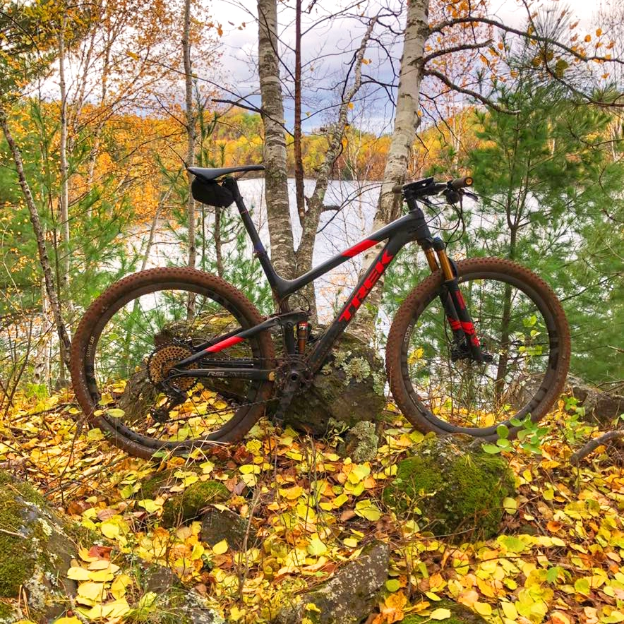 Photo of a bike parked on a bike path on the Cuyuna Mountain Bike Trails surrounded by forest with a lake in the background on a fall day