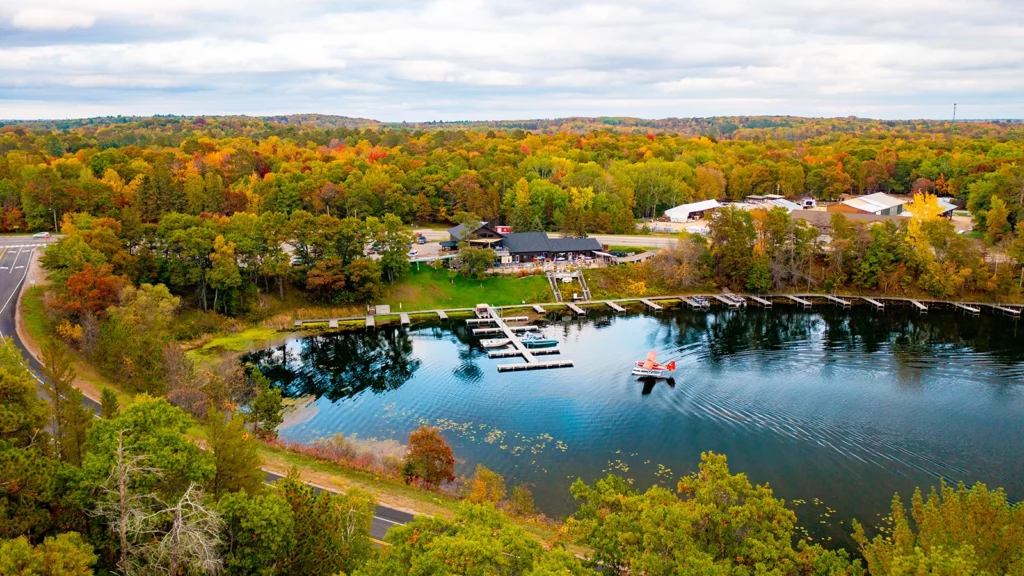 Photo of a lake on a fall day surrounded by forest with docks at the edge of the water and a plane landing on the lake